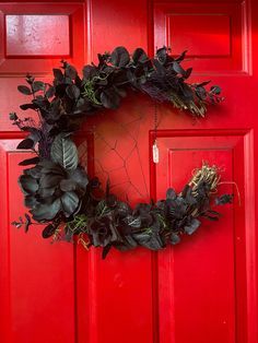 a red door with a wreath hanging on it's side next to a green plant