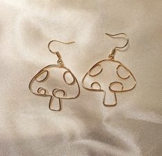 a pair of gold colored earrings on a white fabric background with the image of a mushroom