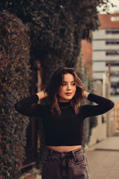 a woman standing on the sidewalk with her hands behind her head and looking at the camera