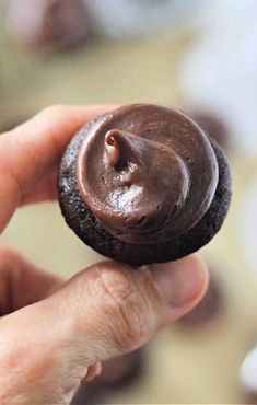 a hand holding a chocolate cookie with frosting on it