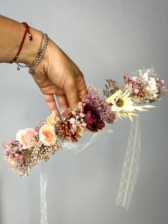 a hand reaching for flowers on top of a glass vase filled with water and greenery