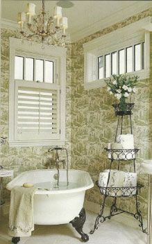 a white bath tub sitting in a bathroom next to a sink and window with shutters