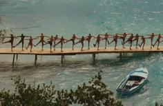 a group of people standing on a long wooden bridge over water with a boat in the foreground