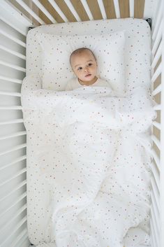 a baby laying in a crib with white sheets and polka dots on it's bed