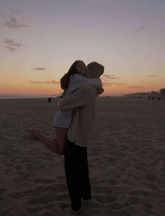 a man holding a woman on the beach at sunset