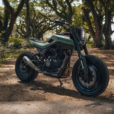 a motorcycle parked on the side of a dirt road in front of some tree's