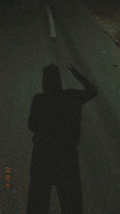 a person standing in the middle of a road at night with their shadow on the ground