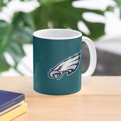 a philadelphia eagles coffee mug sitting on top of a wooden table next to a book