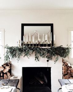 the fireplace is decorated with greenery and candles in front of an empty dining table