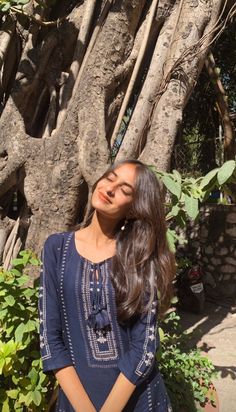 a woman standing in front of a tree with her eyes closed and hands on her hips