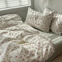 an unmade bed with white sheets and pink flowers on it in front of a window