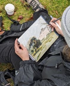 a person sitting on the ground with a painting in their lap and holding a pen