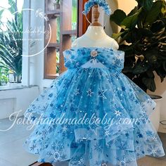 a blue dress with snowflakes on it is displayed in front of a potted plant