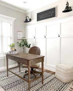 a desk and chair in a room with white paneling on the walls, an area rug that has a black and white design