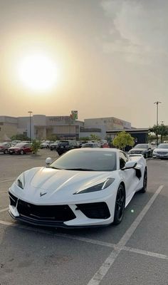 a white sports car parked in a parking lot with the sun setting behind it and buildings