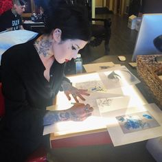 a woman sitting at a table working on some artwork