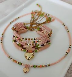 three bracelets with heart charms and beads on a white tray next to a tree