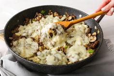 a skillet filled with meat and cheese being stirred by a wooden spoon on top of a table