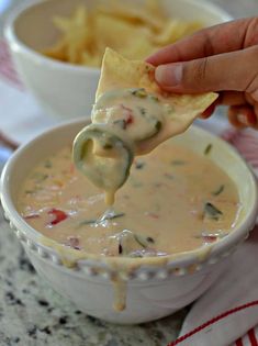 a hand holding a tortilla chip over a bowl of quesadilla dip