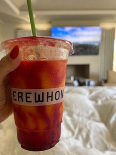 a person holding up a drink in front of a bed with white sheets on it