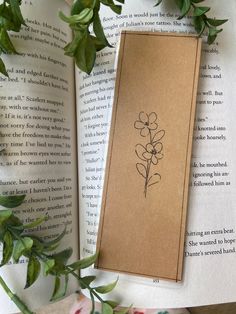 a bookmark with a flower drawn on it sitting next to some leaves and flowers