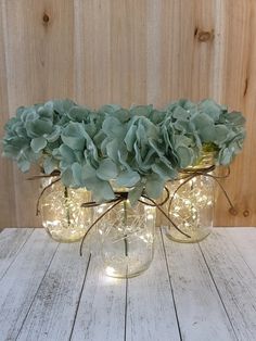 three mason jars filled with green flowers sitting on top of a wooden table