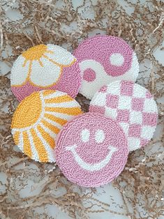 three crocheted coasters sitting on top of some dried up grass, one has a smiley face and the other has a flower