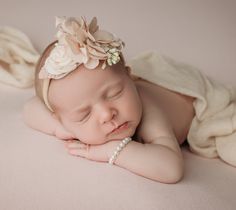 a baby is sleeping with her head on her hands while wearing a flower in her hair