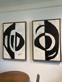 two black and white paintings hanging on the wall next to a wooden dining room table