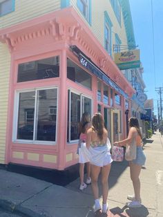 three women in bathing suits standing outside of a pink building with white trim and windows