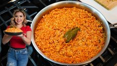 a woman holding a bowl of food in front of an oven with a large pot full of rice