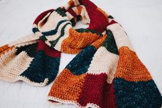 a multicolored knitted scarf laying on top of a white bed coverlet