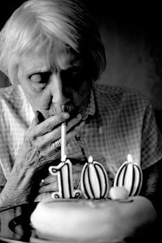 an old woman blowing out the candles on her birthday cake that reads 10 years ago