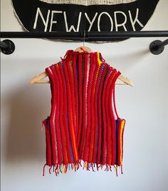 a red sweater vest hanging on a wall next to a sign that says new york