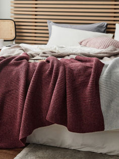 an unmade bed with blankets and pillows on top of it in front of a wooden slatted headboard