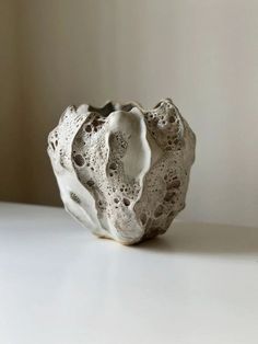 a white vase sitting on top of a table next to a wall and window sill