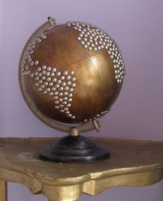 a gold colored globe sitting on top of a wooden table next to a purple wall