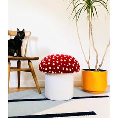 a cat sitting on a chair next to a mushroom shaped stool and potted plant