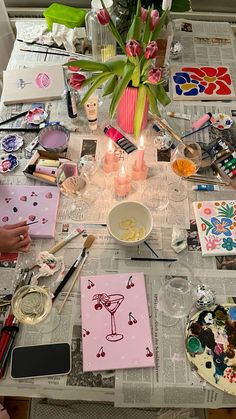 the table is covered with art supplies and flowers in vases, cards, candles, and other items