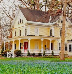 a large yellow house sitting in the middle of a field with blue flowers on it