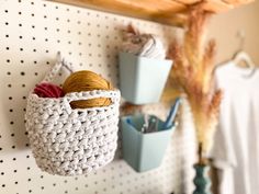 there is a crocheted basket hanging on the wall with yarn and scissors in it