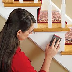 a woman in red shirt holding a book near stair railing and carpeted area with white handrails