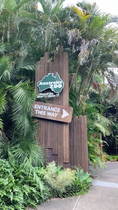 the entrance sign to an attraction park with palm trees and foliage around it, along with a directional arrow pointing in opposite directions