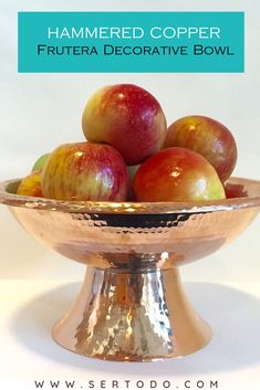 a metal bowl filled with apples on top of a white tablecloth and text overlay reads hammered copper fruiter decorative bowl