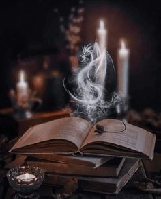 an open book sitting on top of a pile of books next to candles and a candle holder