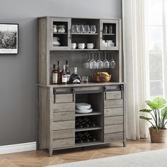 a wooden cabinet with wine glasses and bottles on the top, next to a potted plant