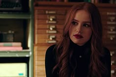 a woman with long red hair standing in front of a book shelf