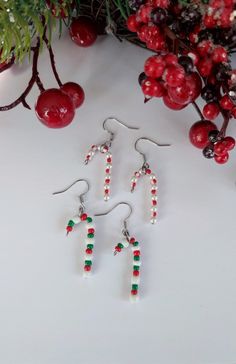 two red and green beaded earrings next to some berries on a white table with evergreen branches