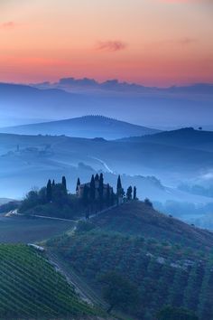 the rolling hills and valleys are covered in mist as the sun sets over an italian countryside