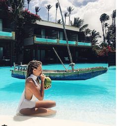 a woman sitting on the edge of a swimming pool while holding a green object in her hand